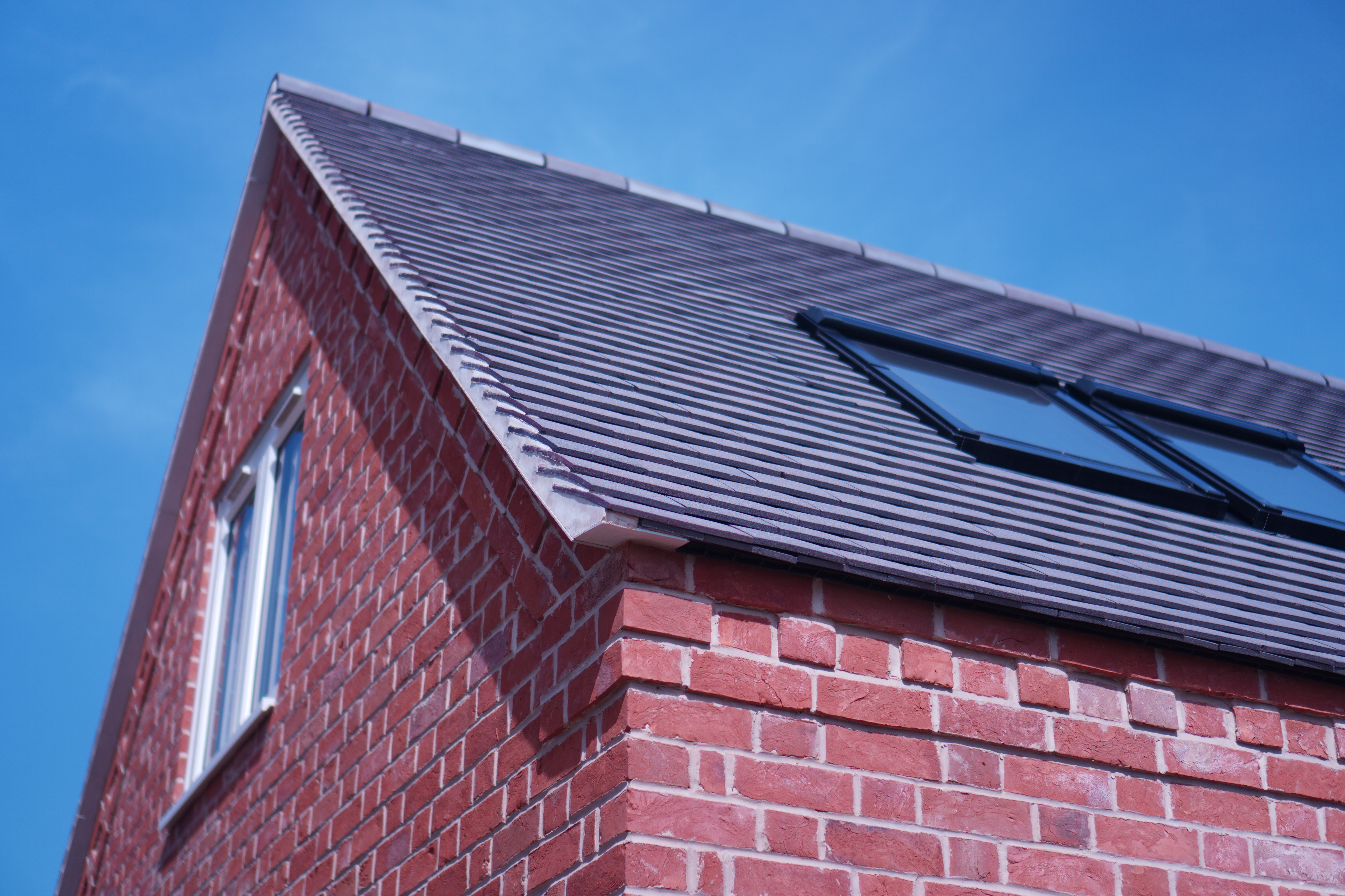 Corner view of a completed grey tiled pitched roof with Velux skylights on a UK red brick property