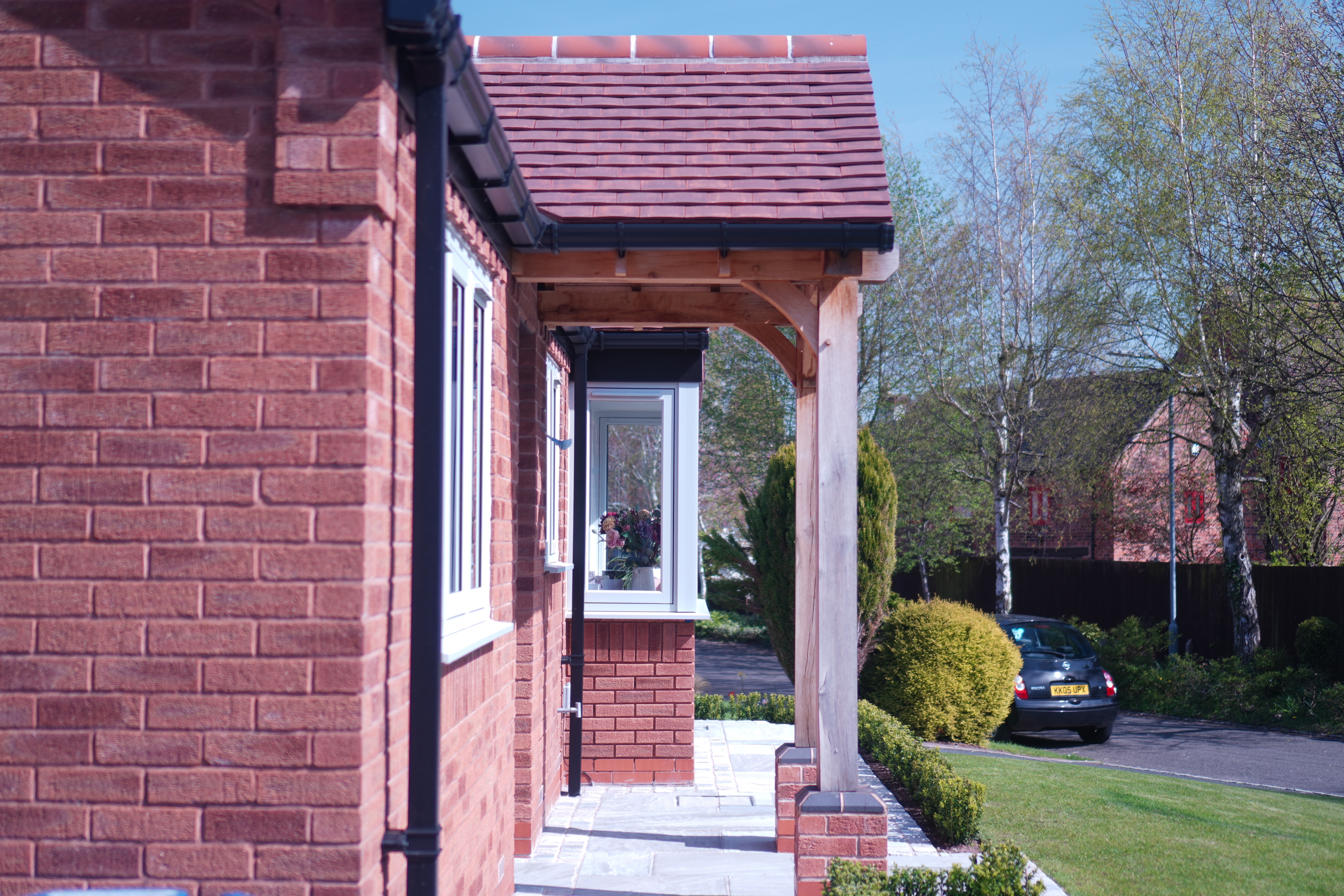 Side view of UK red brick bungalow showing tiled roof canopy and black uPVC fascias and guttering