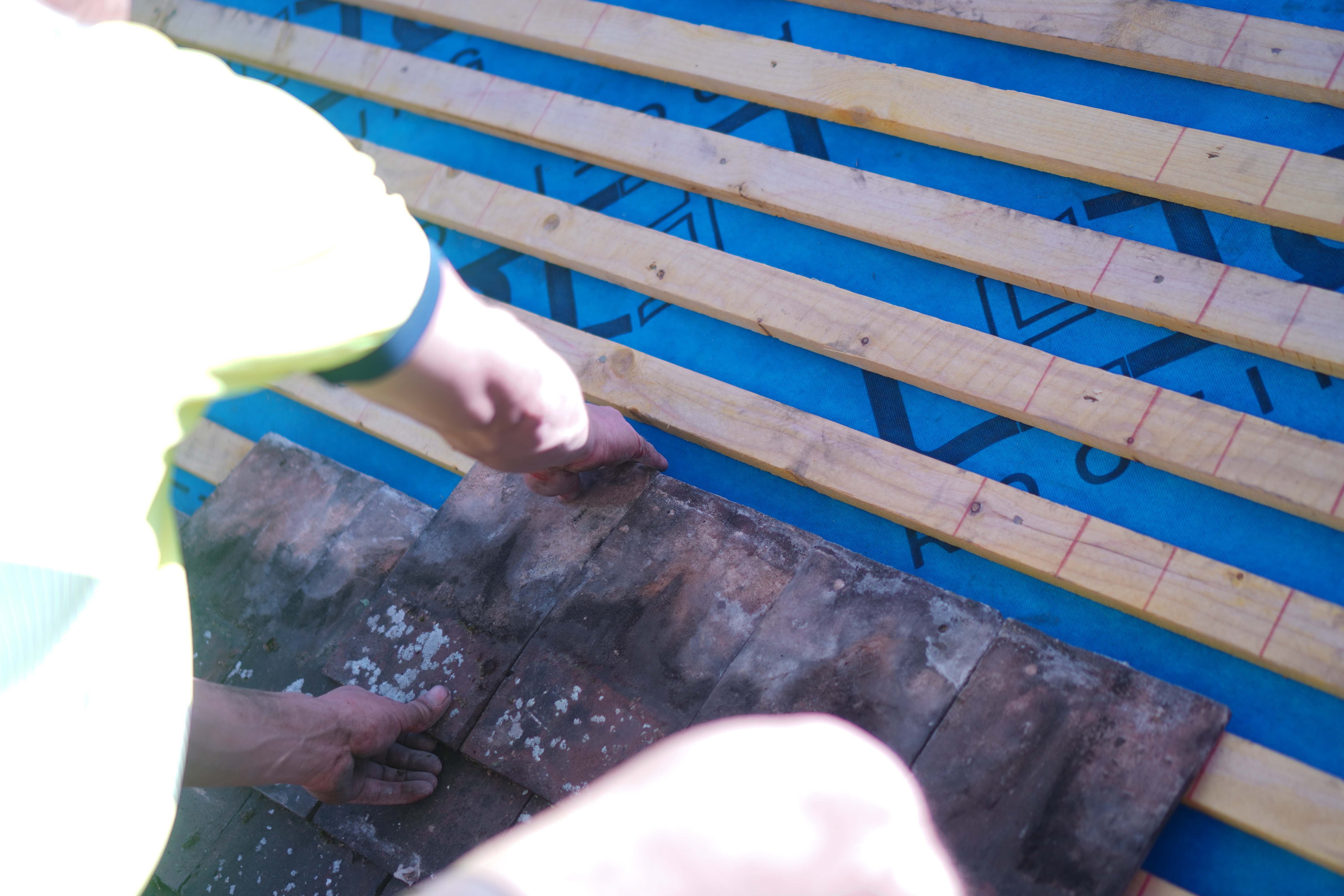 Skilled hands carefully placing clay tiles on new roofing felt and battens