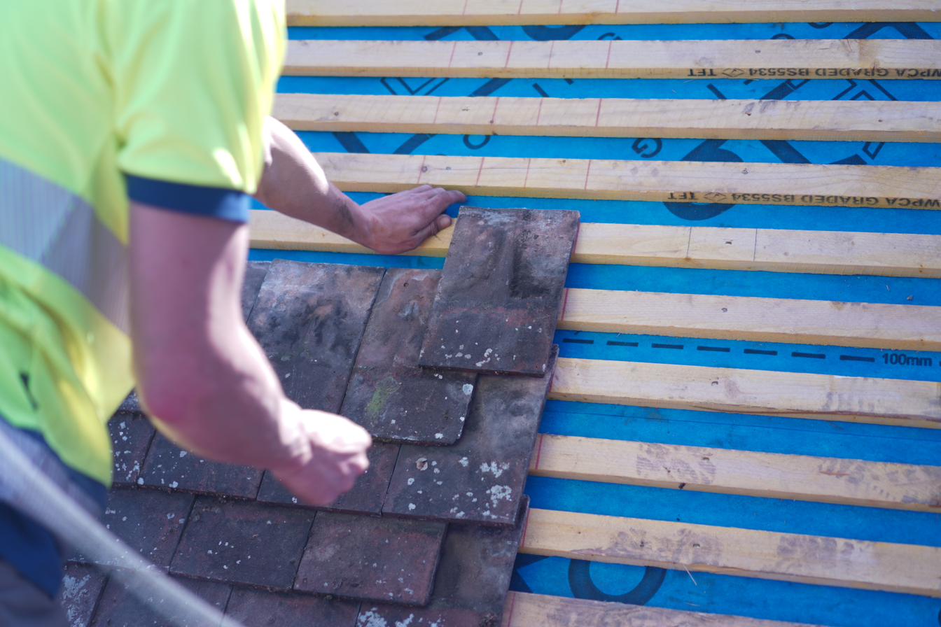 Careful tile work in progress — new battens and underfelt with tiles being laid by hand