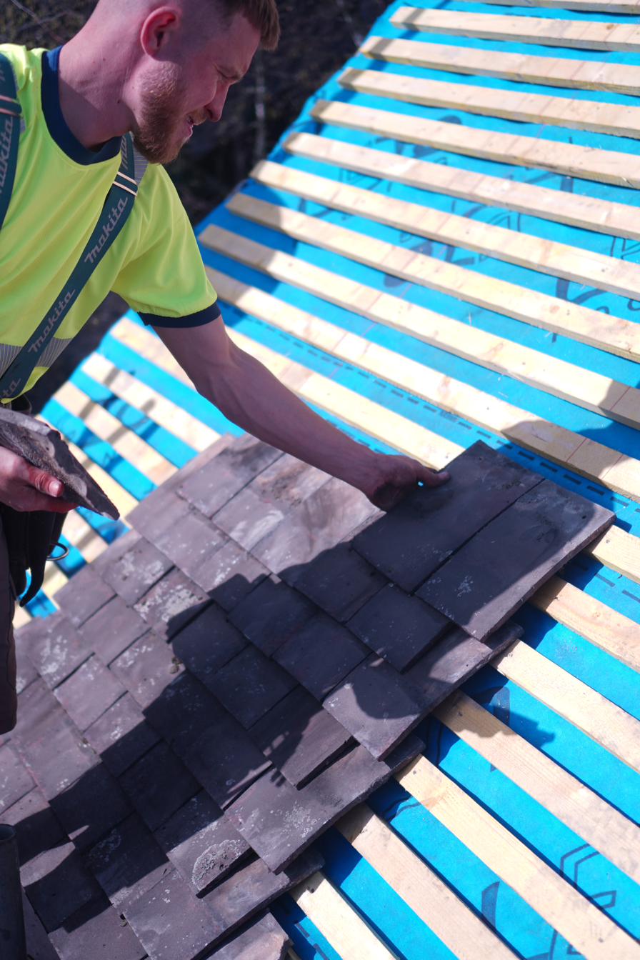 Roofer carefully laying individual slate tiles during a roof repair